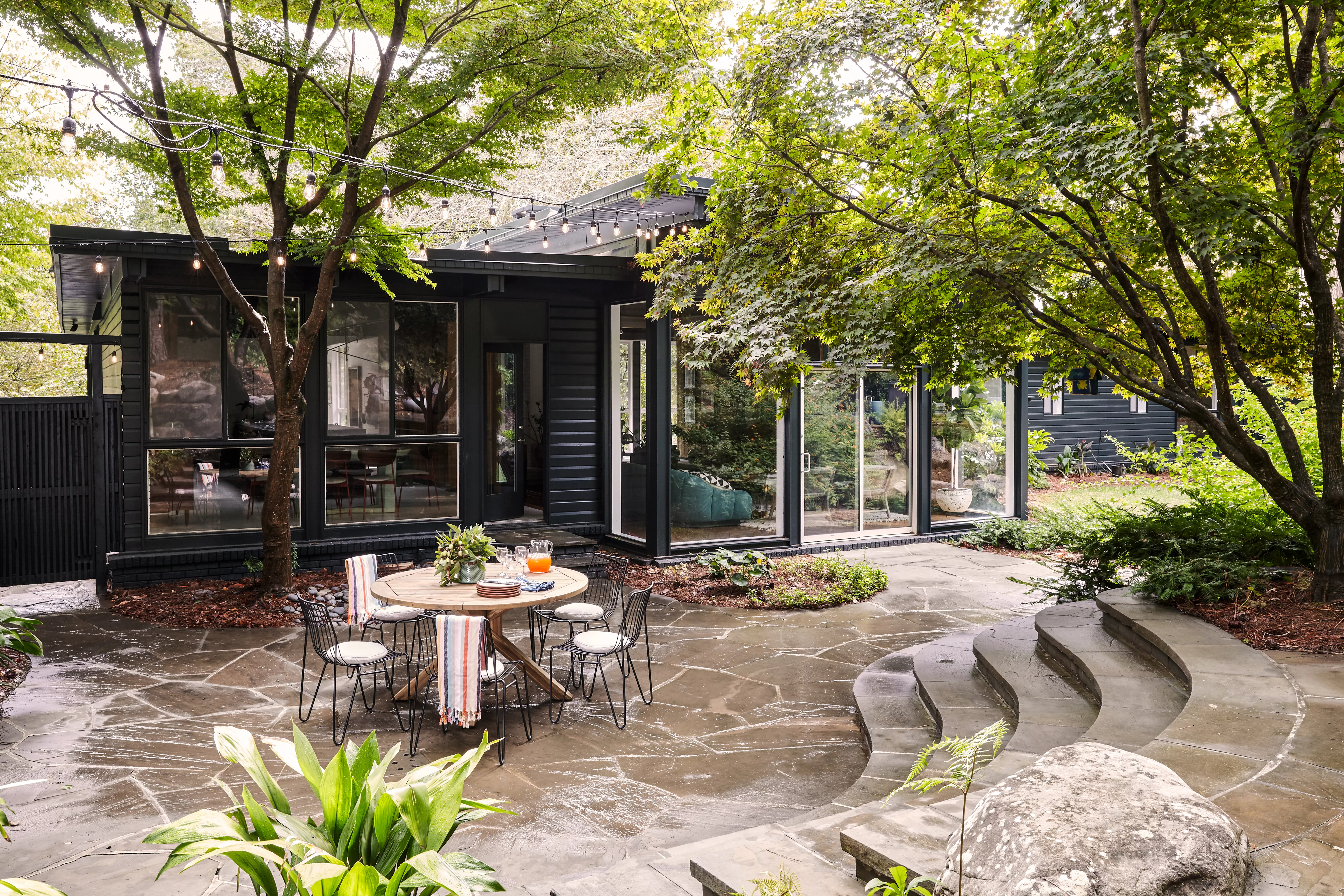 nteriors, exteriors - back patio with round dining table and black metal chairs, string lights and concrete stairs