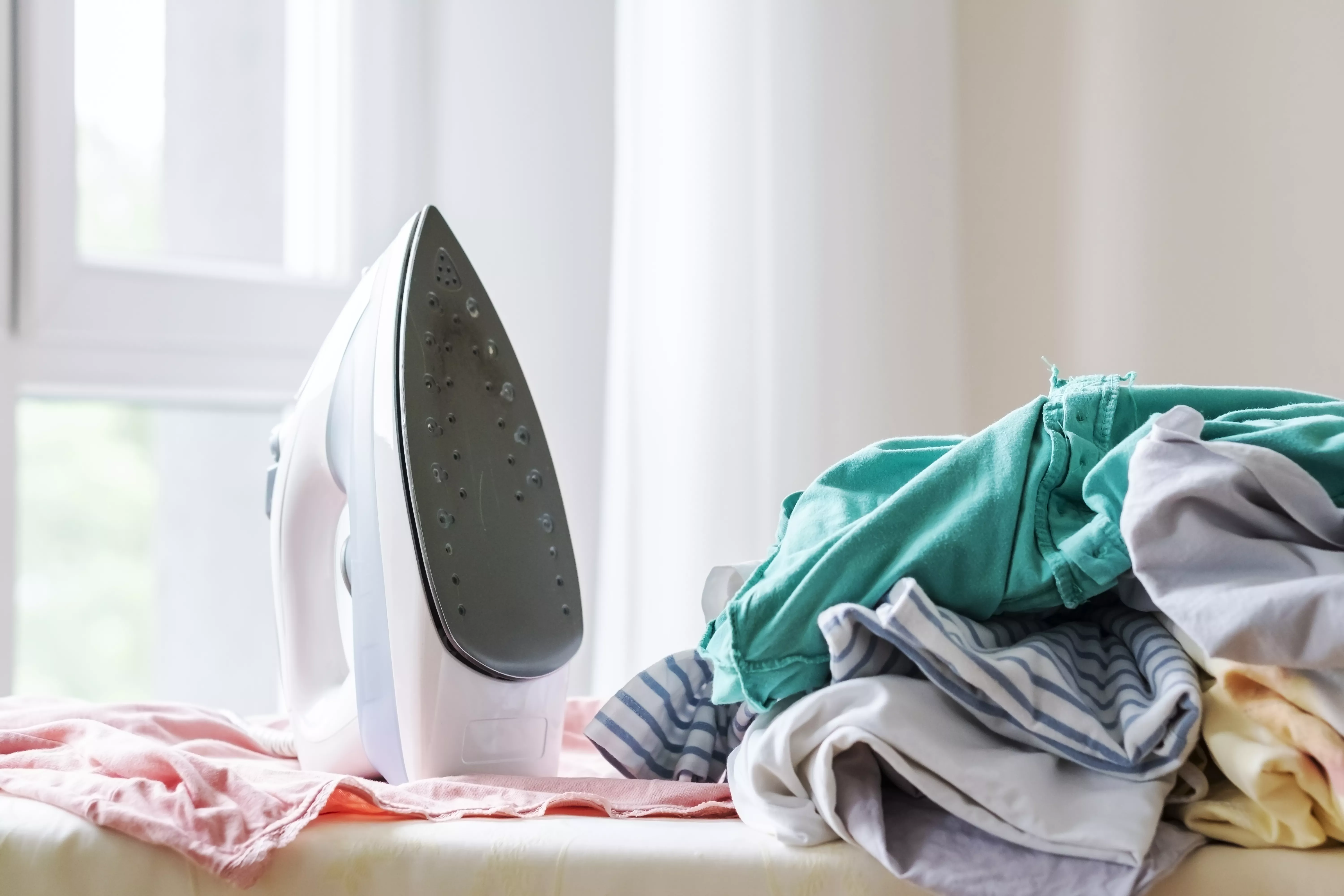 iron on ironing board with wrinkled clothes