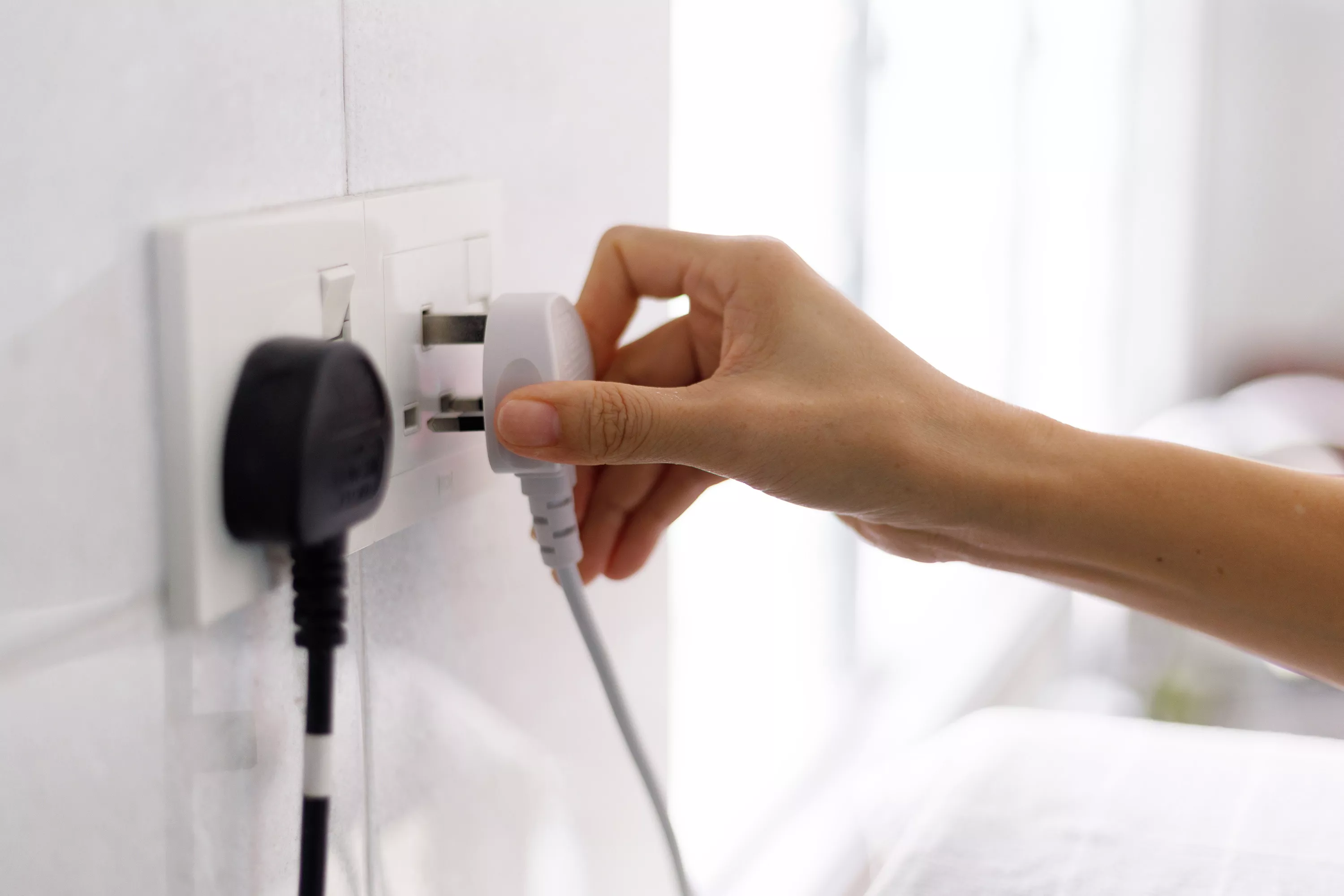 person unplugging cord from outlet on white wall