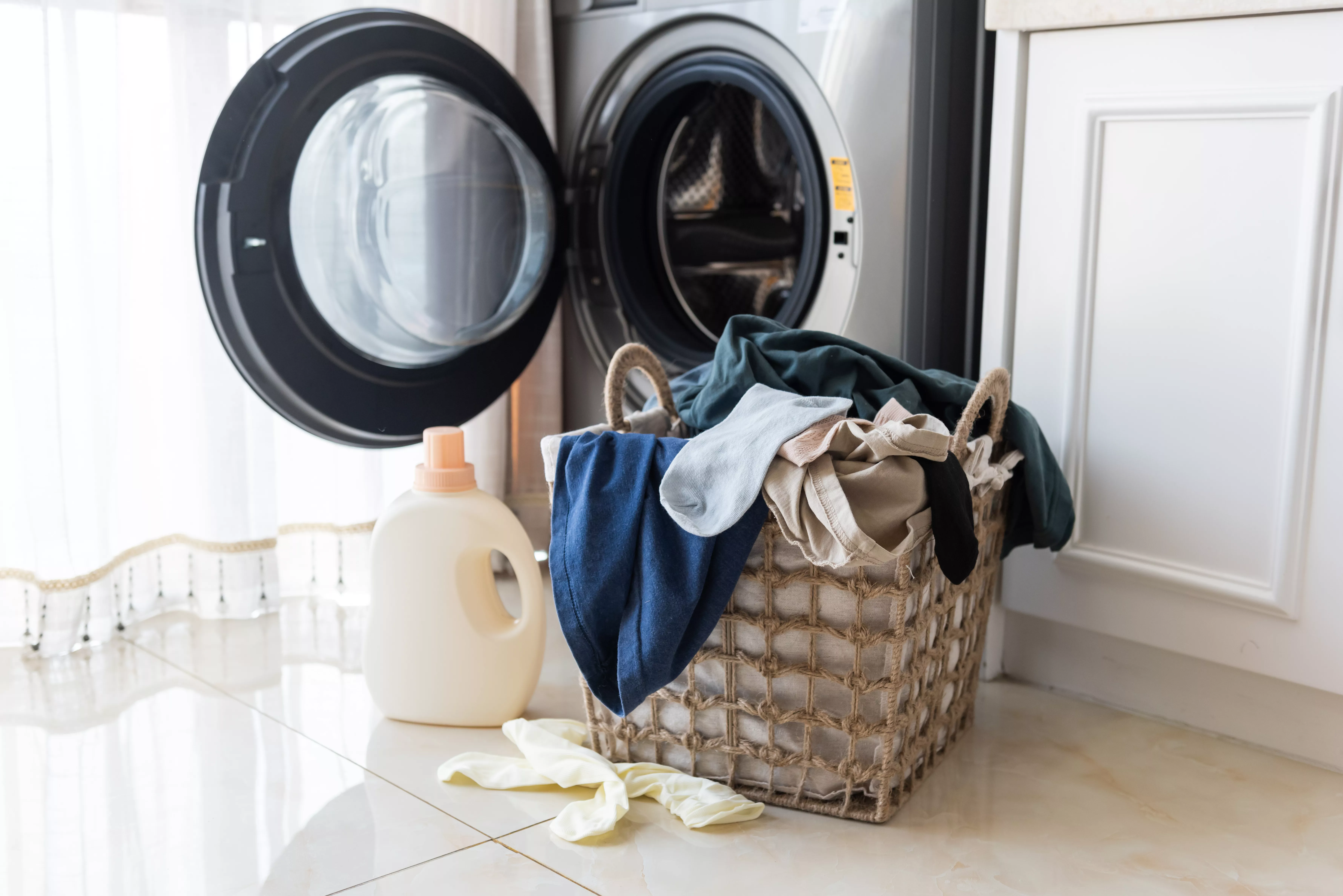 A laundry basket full of clothes sitting on the floor in front of a washer.