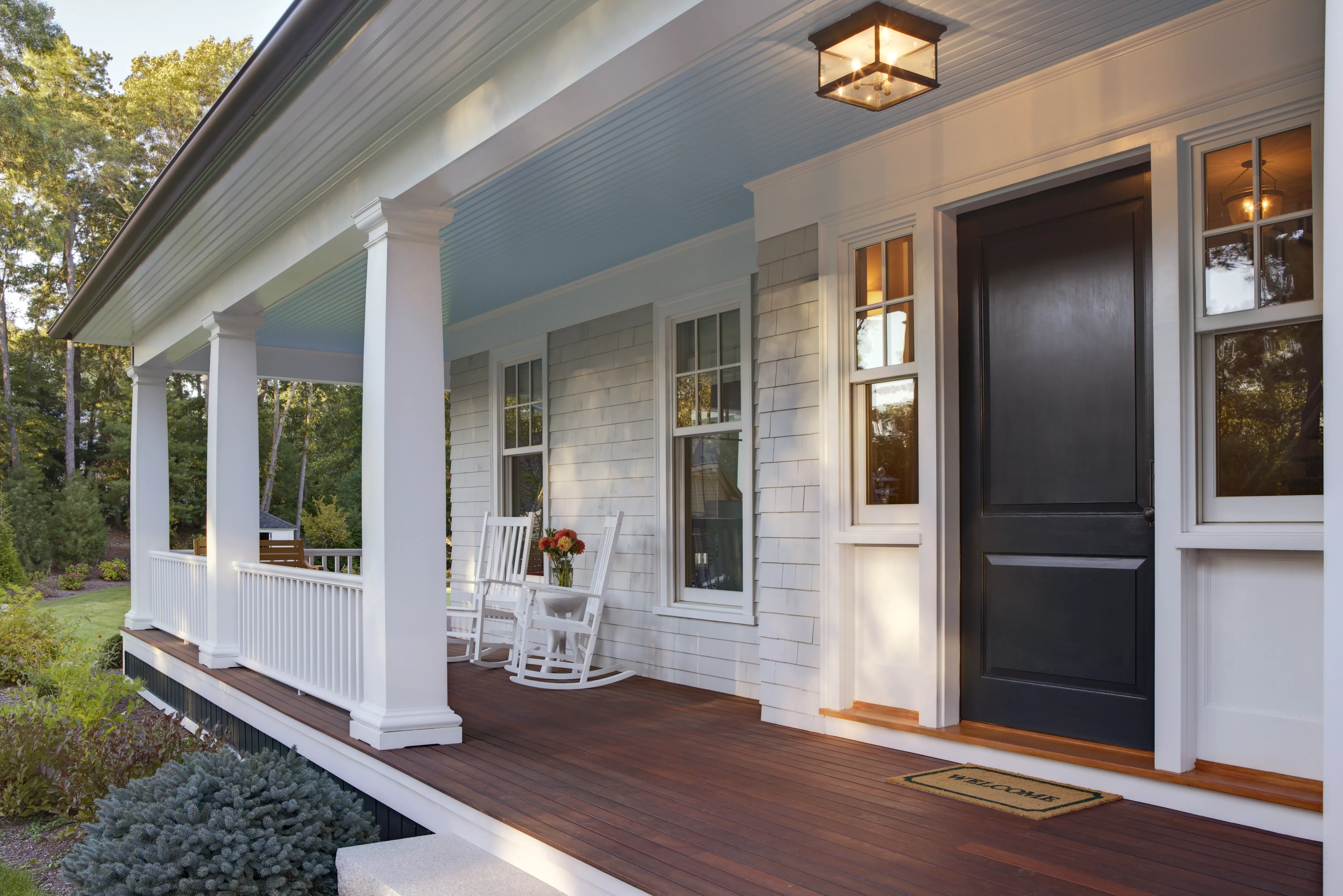 Front porch of custom home with front door and two rocking chairs in soft sunlight.
