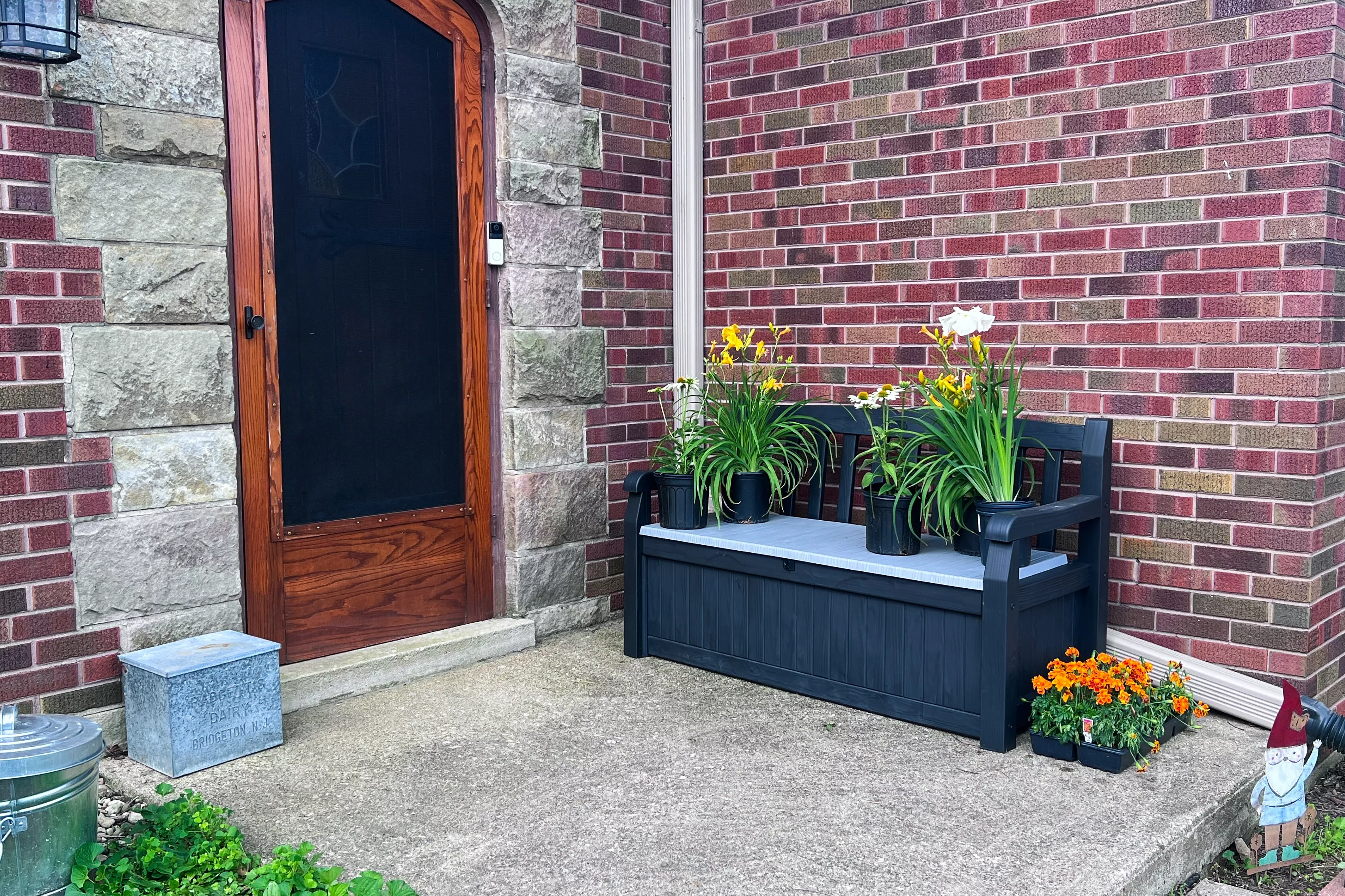 A closed Keter Solana 70-Gallon Outdoor Storage Bench near doorway with plants resting on top