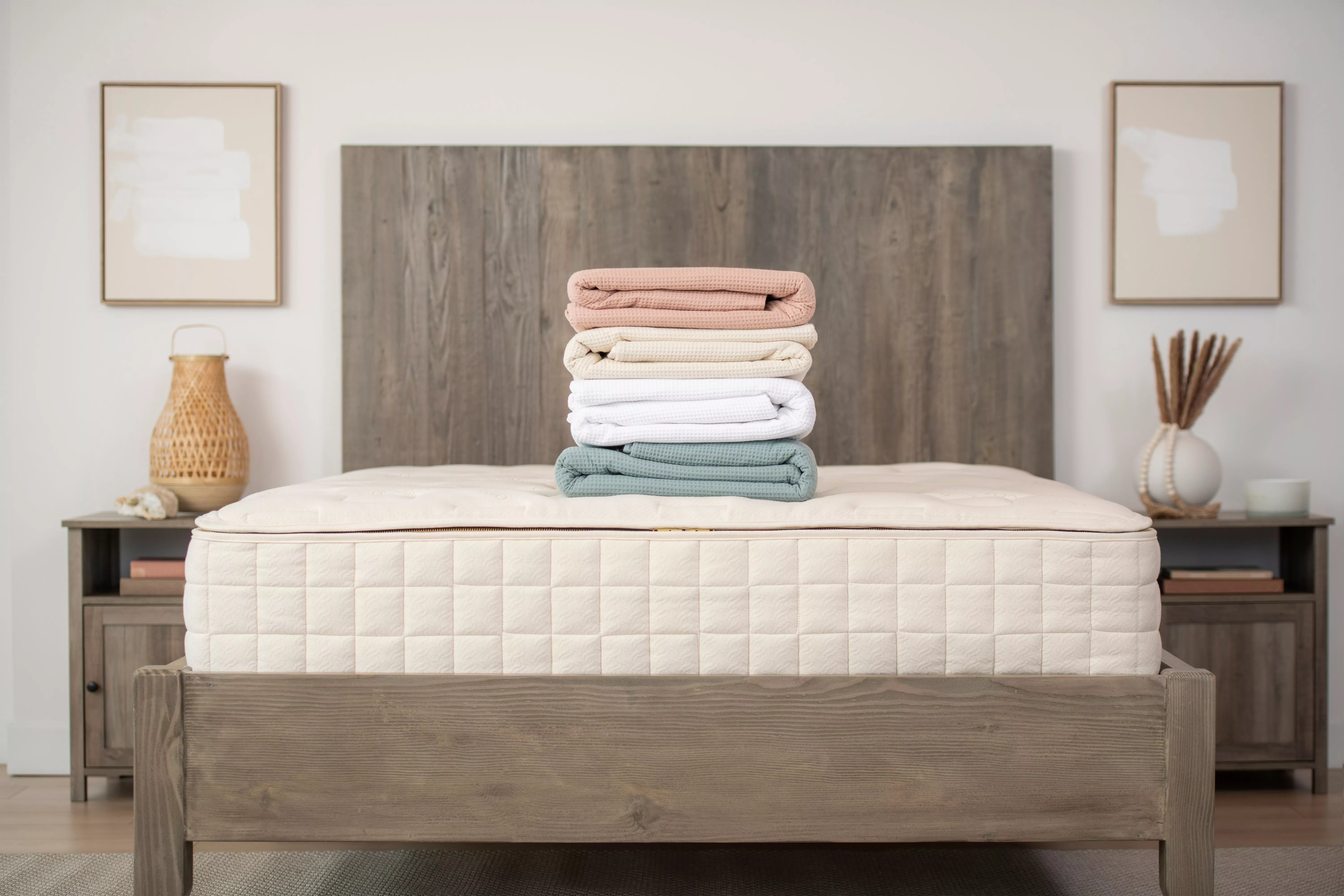 Naturepedic Hotel Bedding stacked on top of a mattress next to night tables and paintings